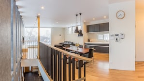 A modern kitchen with dark cabinets, a wooden dining table, and a built-in oven. - Ikigai (Kutchan)