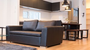 A modern living room with a dark leather sofa, a dining table, and a kitchen in the background. - Ikigai (Kutchan)