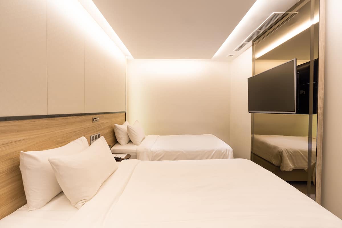 Quarto de hotel com duas camas, uma televisão presa à parede e um guarda-roupa com espelho.
