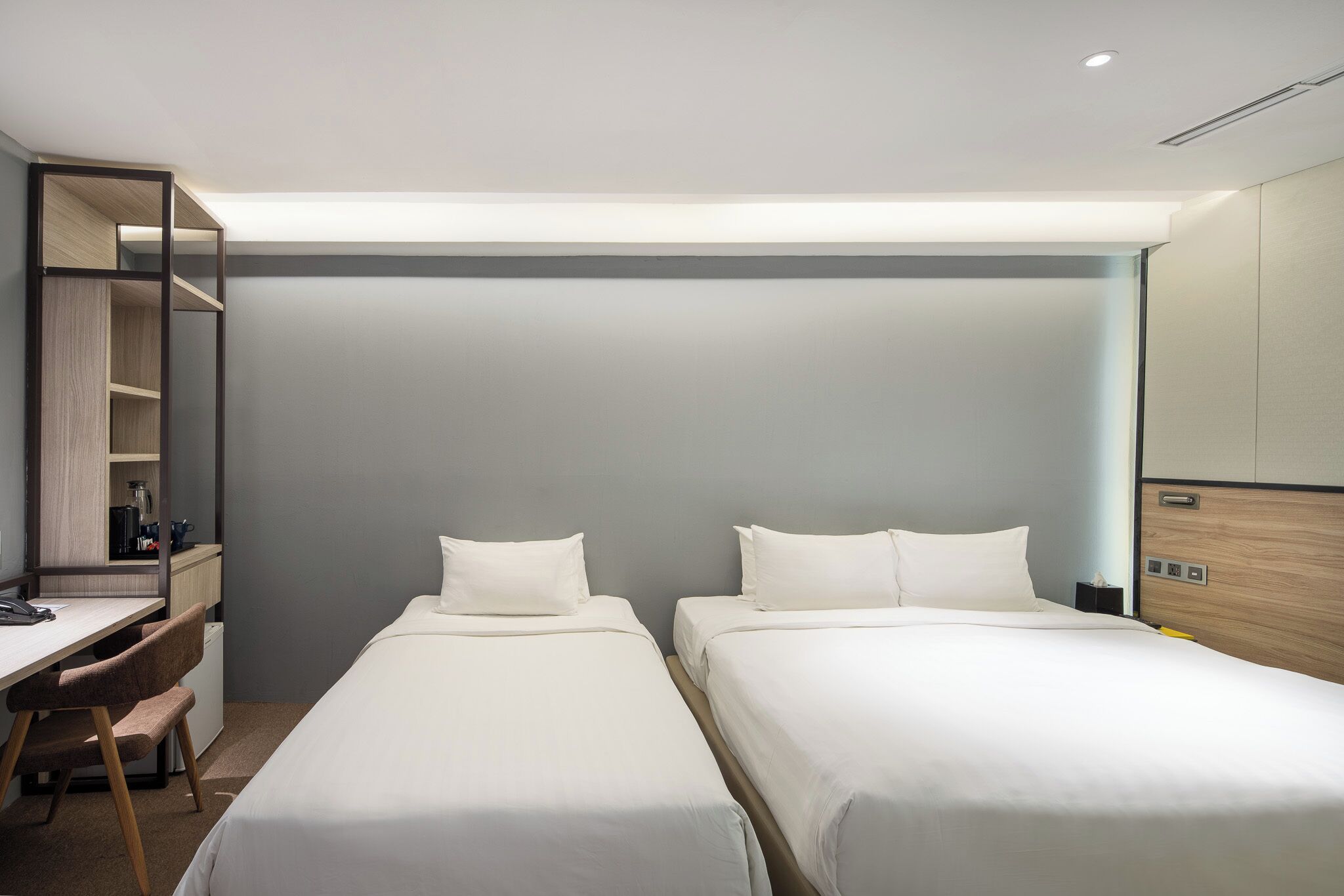Habitación de hotel con dos camas individuales, un escritorio con silla, una mesita de noche y un espejo.