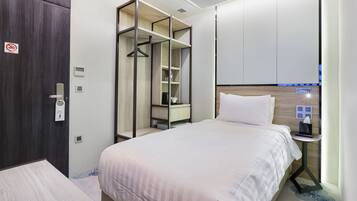 A hotel room with a bed, a wardrobe, a bedside table with a lamp, and a wall-mounted control panel.