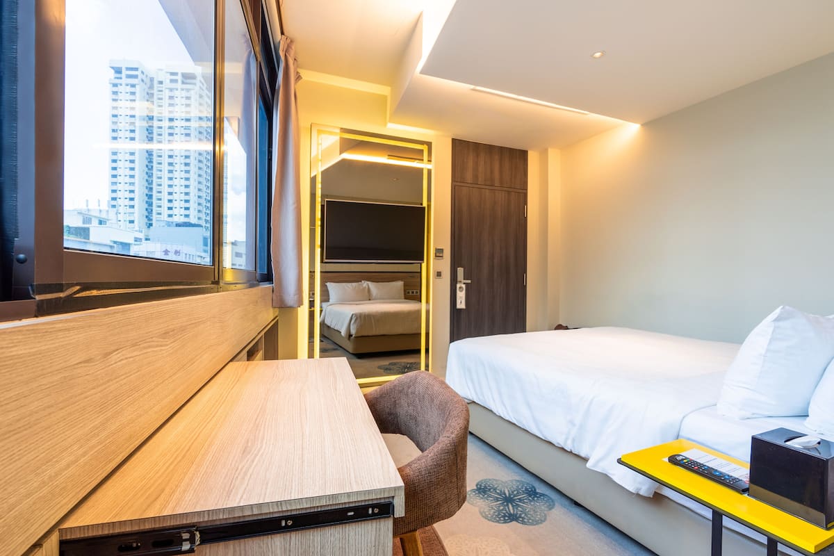 Quarto de hotel com cama, escrivaninha, cadeira e pequena mesa com controle remoto.