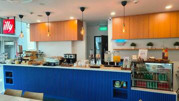 A breakfast bar with coffee machines, a juice dispenser, and a refrigerator with beverages.
