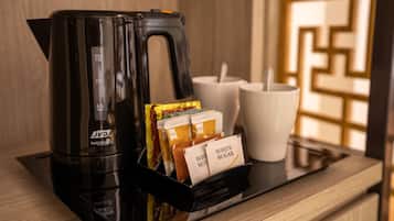 A black coffee maker with a timer, a tray with sugar packets, and two white mugs on a wooden surface.