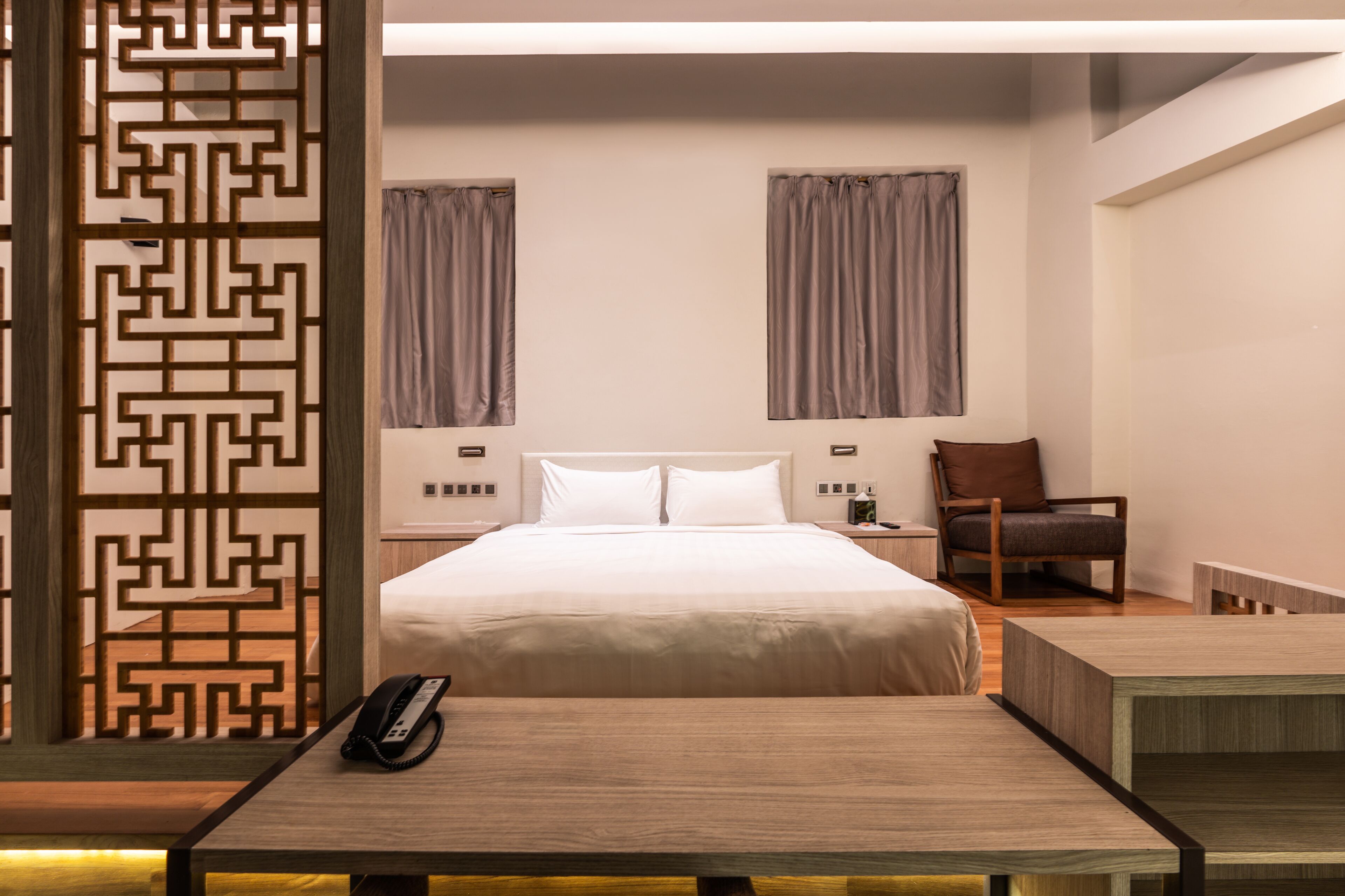 A modern hotel room with a large bed, a wooden nightstand, a chair, and a desk.