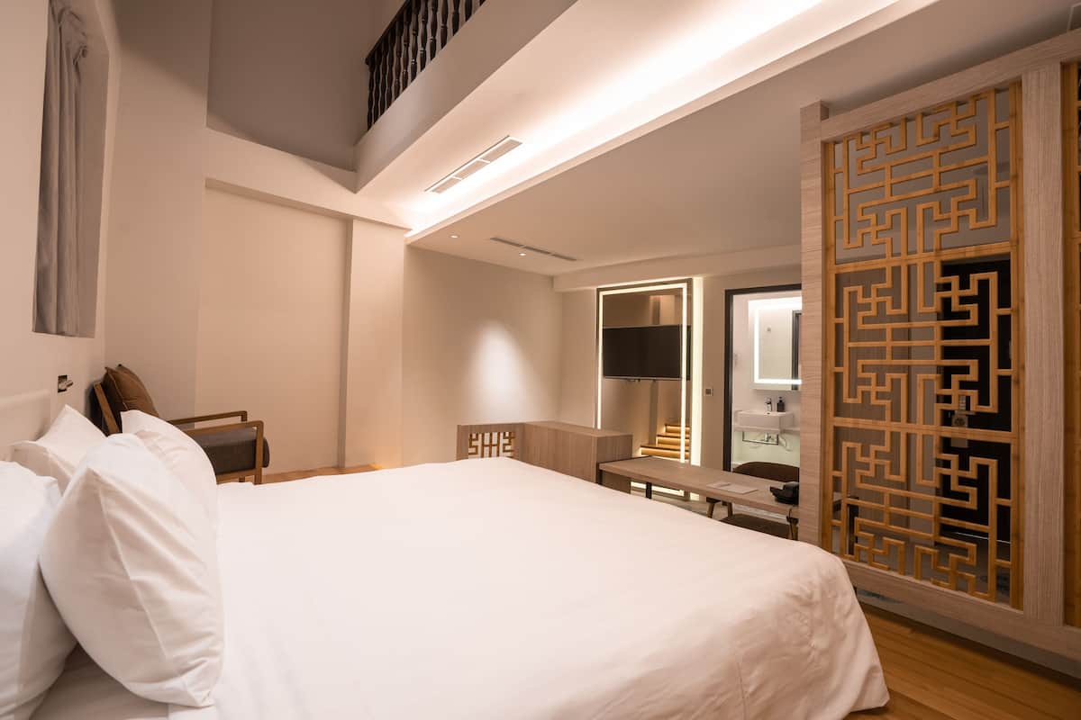 Quarto de hotel moderno com uma cama grande, uma escrivaninha, um espelho e um painel decorativo de madeira.
