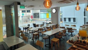 Interior de restaurante con varias mesas y sillas, un ventanal que ofrece vista a la calle y lámparas colgantes.