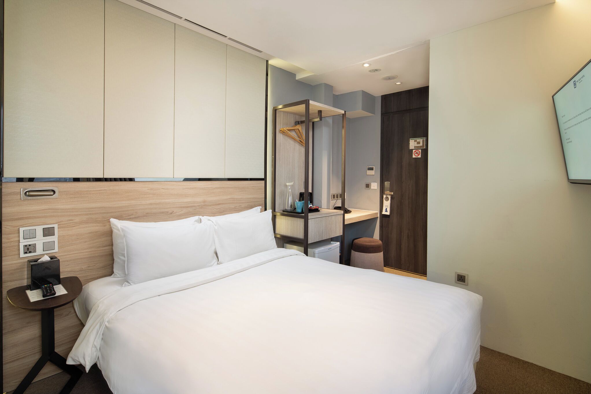 Una habitación de hotel moderna con una cama grande, una mesita de noche con un teléfono y una lámpara, un espejo y un armario.