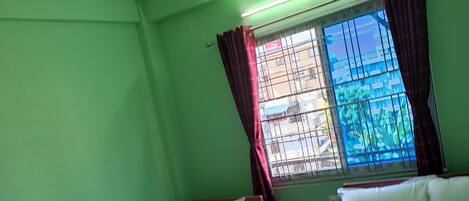 Una habitación con dos camas individuales, ventilador de techo, aire acondicionado y una ventana con barrotes y cortinas.