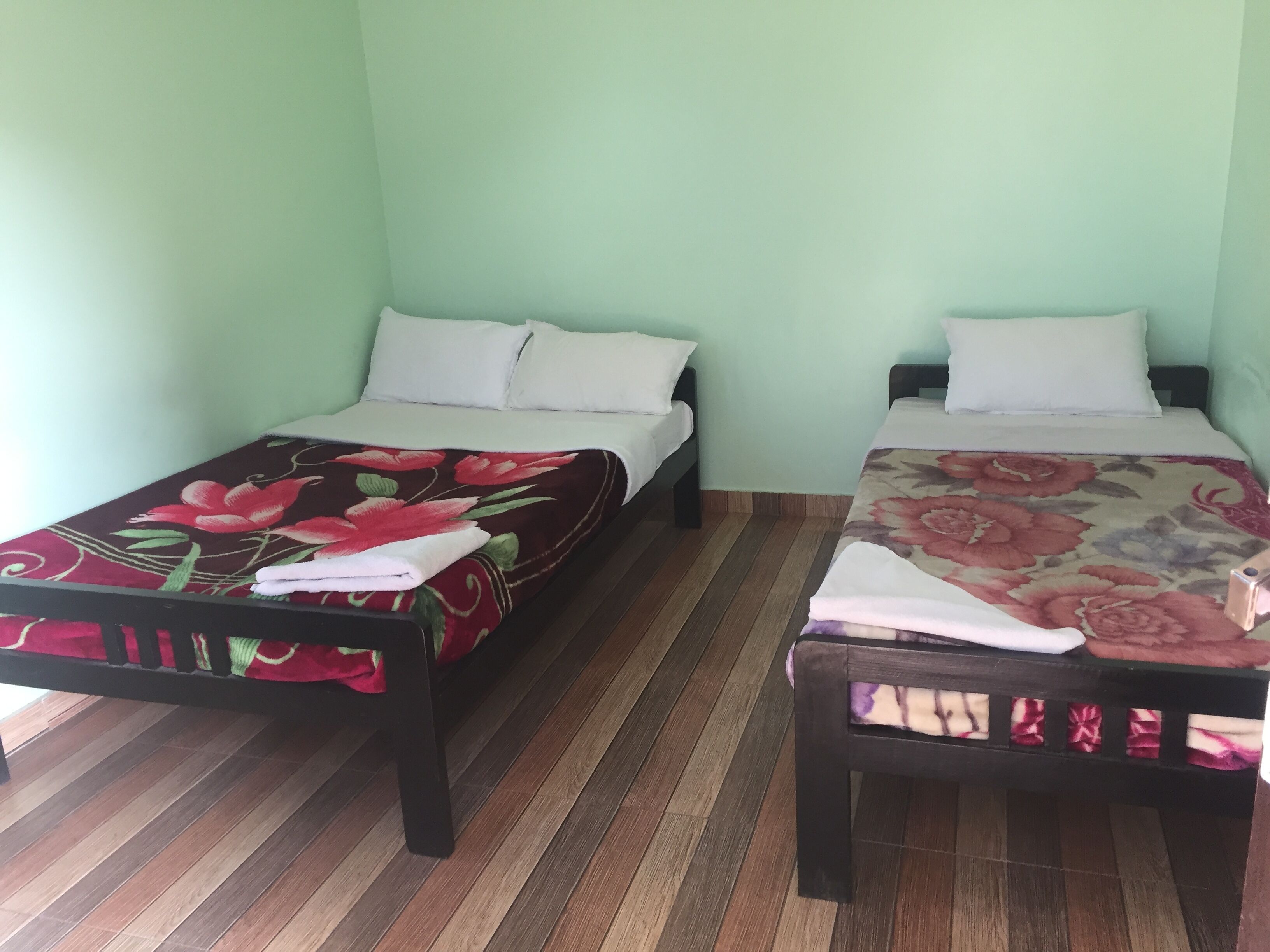 Een kamer met twee éénpersoonsbedden, elk met een bloemenprint sprei en witte kussens. De muren zijn lichtgroen en de vloer is van hout.
