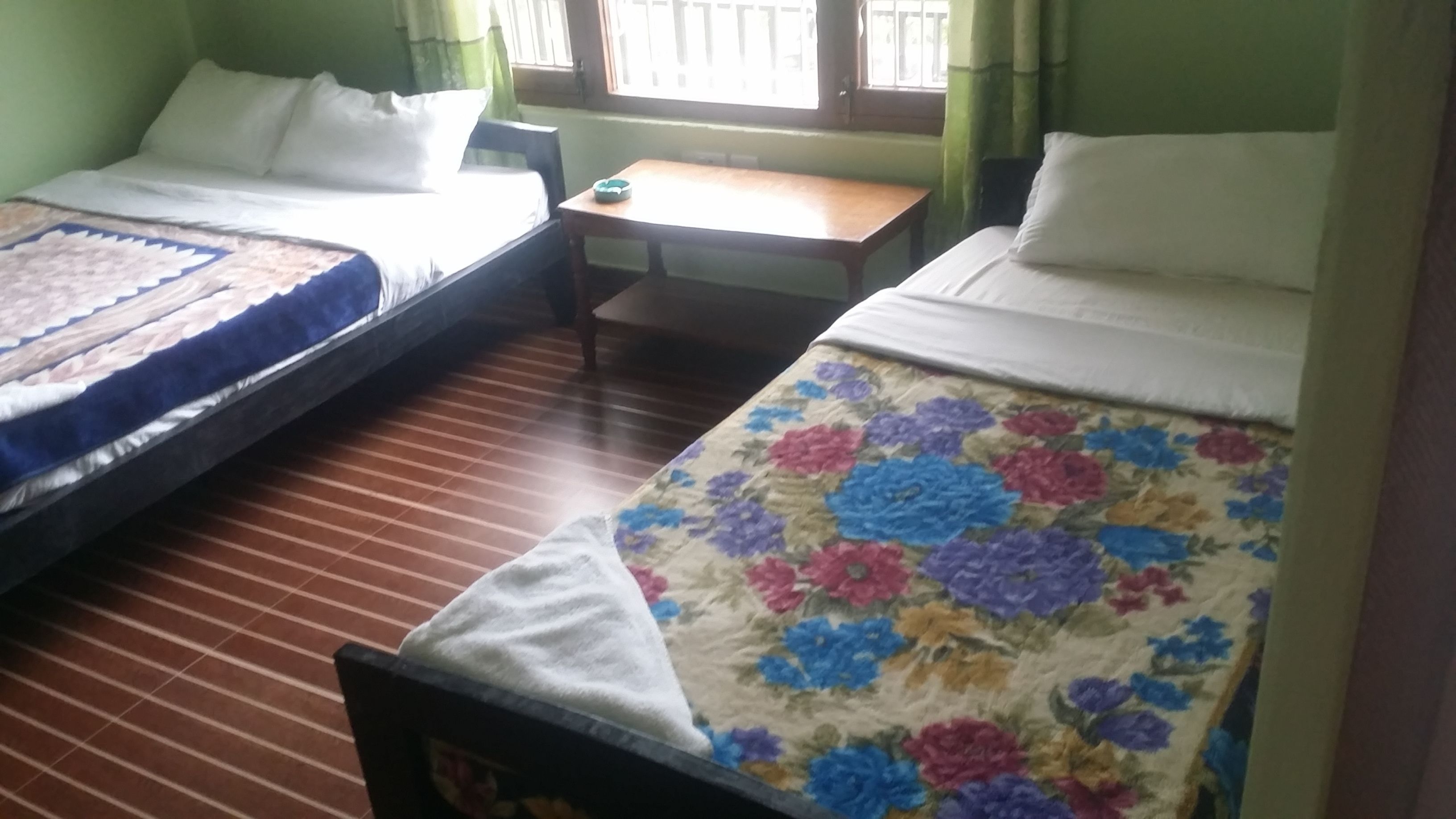 Una habitación con dos camas, una mesita y un ventanal con cortinas.