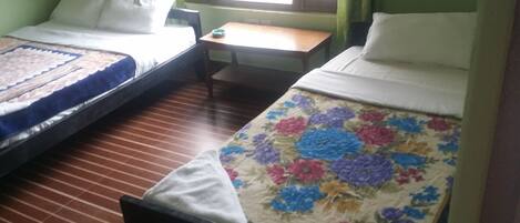 Una habitación con dos camas, una mesita y un ventanal con cortinas.