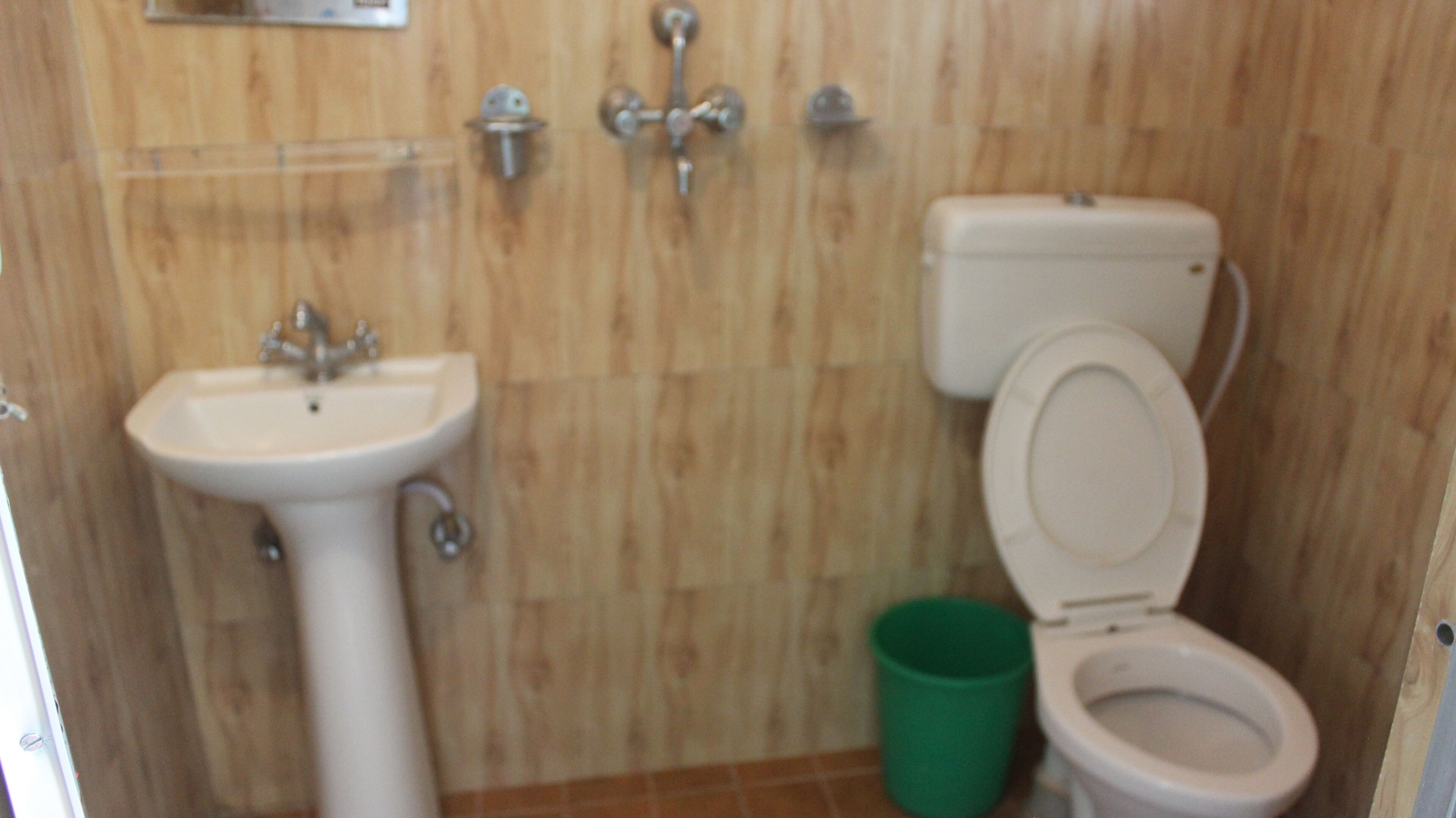 A small bathroom with a sink, toilet, and a green trash bin.