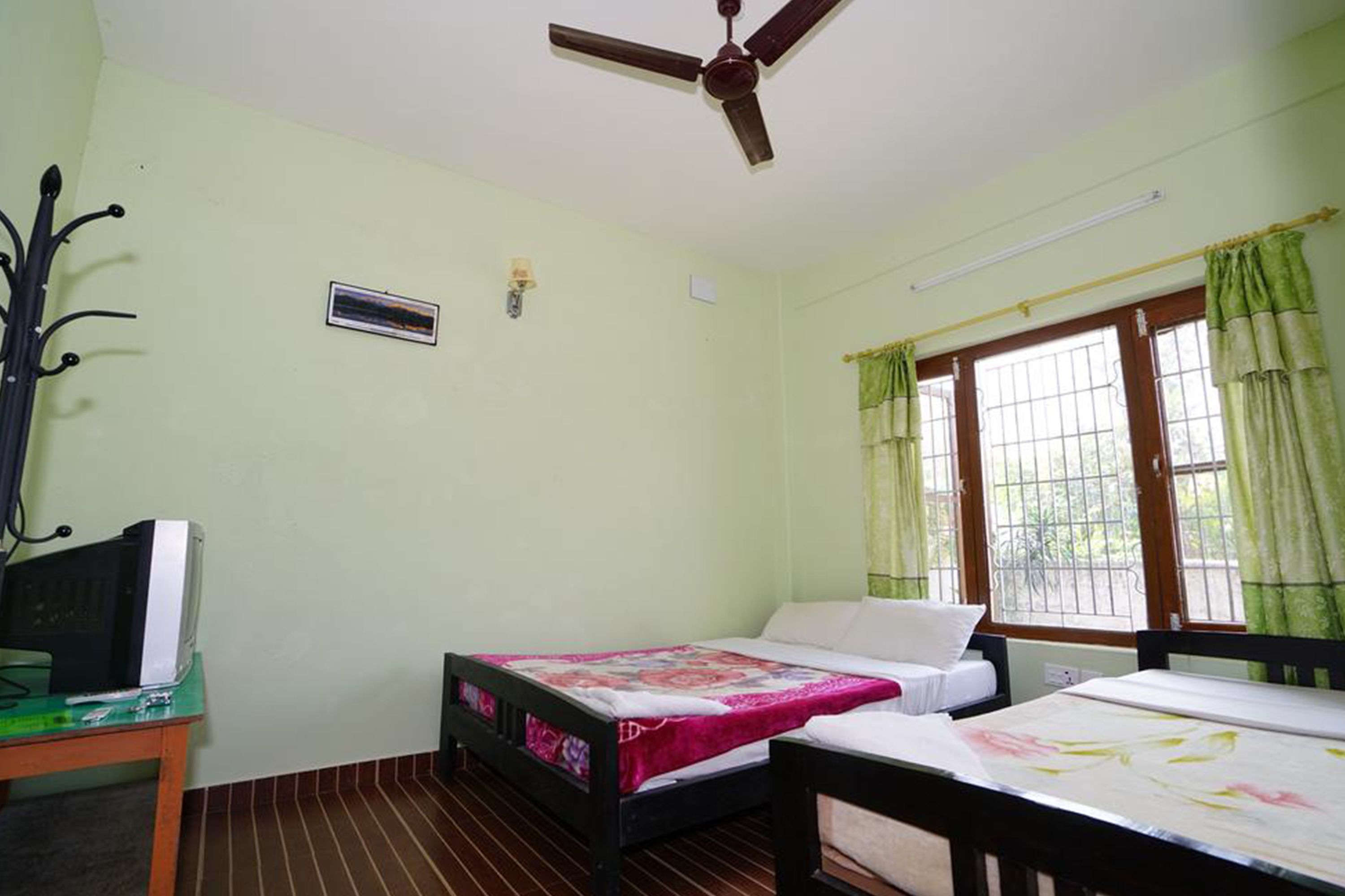 A room with a bed, a desk, a ceiling fan, and a window with curtains.