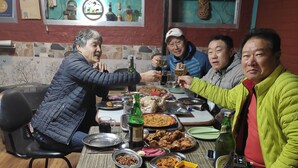 A group of people sitting around a table with various dishes and drinks, in a room with a sign reading "Harry Guest House, Pokhara, Nepal". - Harry Guest House & Restaurant (Pokhara)