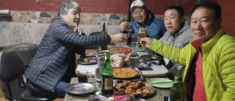 Un grupo de personas sentadas alrededor de una mesa con diferentes platos y bebidas, en una habitación con un cartel que dice 'Harry Guest House, Pokhara, Nepal'.