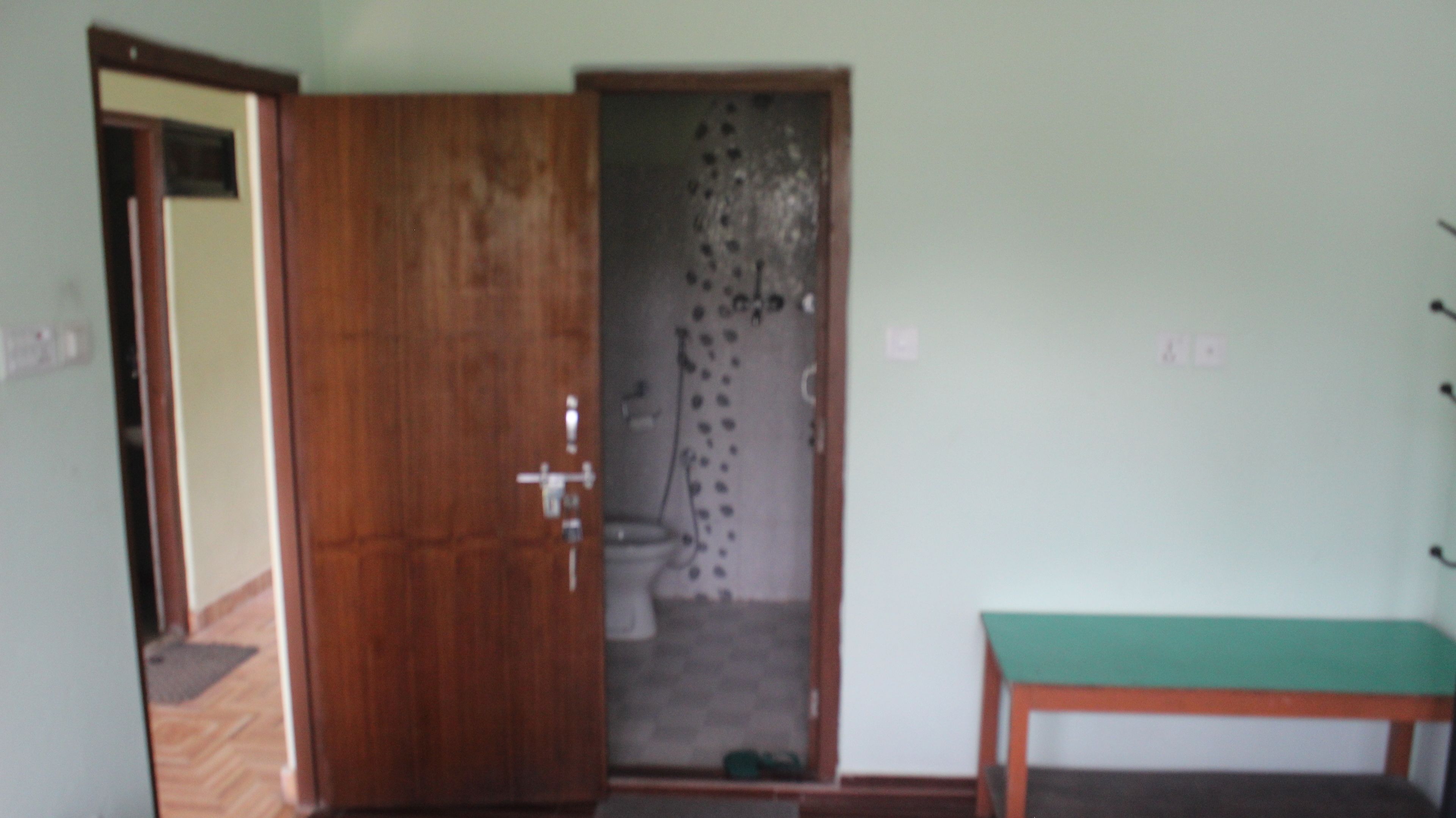 A room with a wooden door, a green bench, and a shower area.