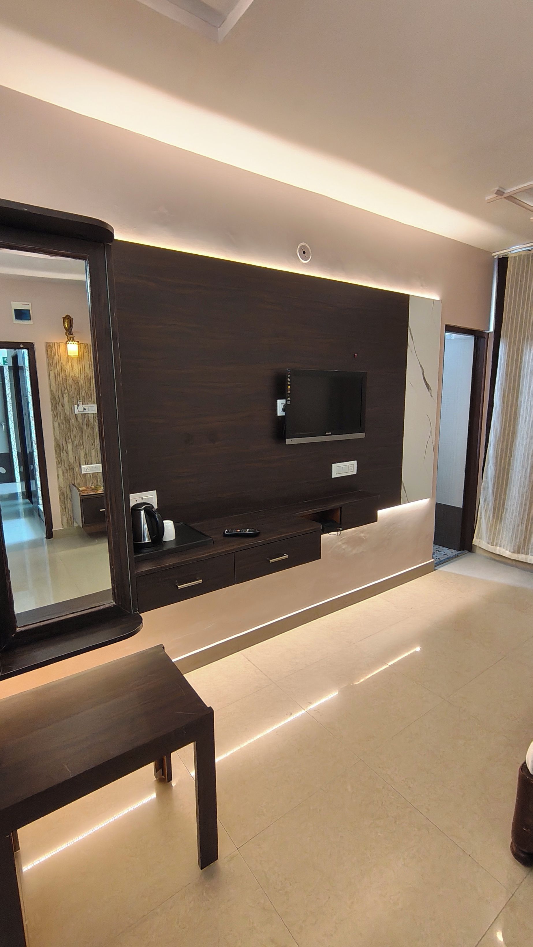 Una sala moderna con un televisor de pantalla plana, un espejo grande y un mueble de entretenimiento de madera.