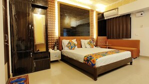 A hotel room with a large bed, a wardrobe, a nightstand, an air conditioning unit, and a window with curtains. - Omni Plaza (Jodhpur)