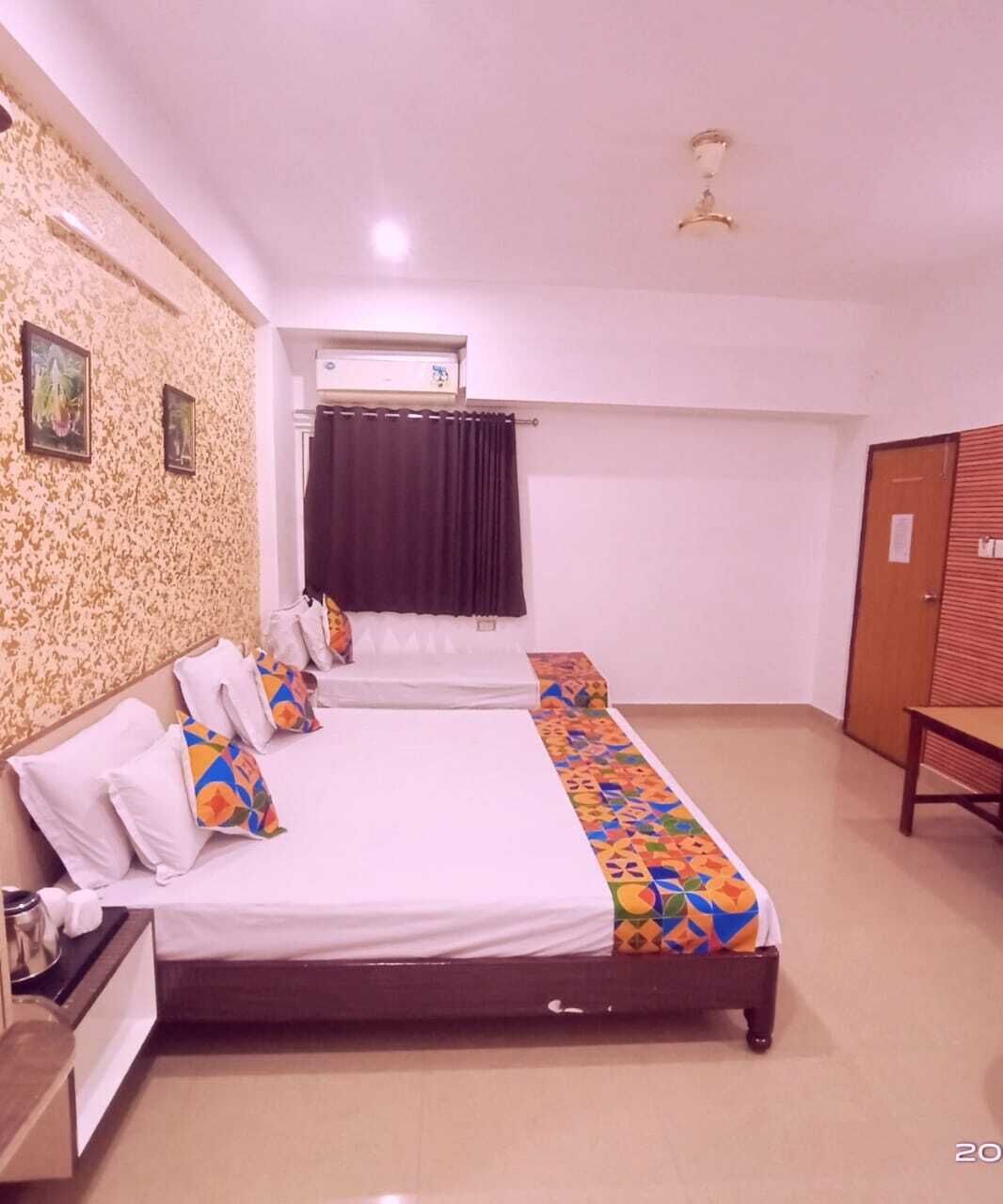 A hotel room with a large bed, a small table, a wardrobe, and an air conditioning unit.