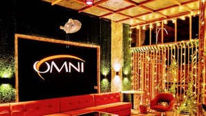A modern interior with a black wall featuring the 'OMNI' logo, a red sofa, a glass coffee table, and a wooden floor. - Omni Plaza (Jodhpur)