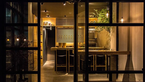 A dimly lit interior with a dining area, kitchen, and a view through a glass door. - AET HOTEL (Tokyo)