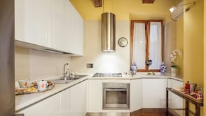 A kitchen with white cabinets, a stainless steel range hood, a built-in oven, and a window with curtains. - Impero Vaticano Navona Apartment (Rome)