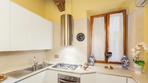 A kitchen with white cabinets, a stainless steel range hood, a gas stove, a sink, and a clock on the wall. - Impero Vaticano Navona Apartment (Rome)