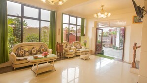 A spacious living room with a sofa, armchairs, and a coffee table. Large windows offer a view of the outdoors. - Inle Apex Hotel (Nyaungshwe)