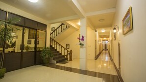 A hotel lobby with a staircase, potted plants, and a reception desk. - Inle Apex Hotel (Nyaungshwe)