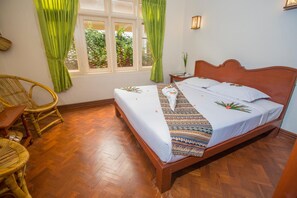 A neatly arranged bedroom with a wooden bed, green curtains, a wicker chair, and a small table. - Inle Apex Hotel (Nyaungshwe)