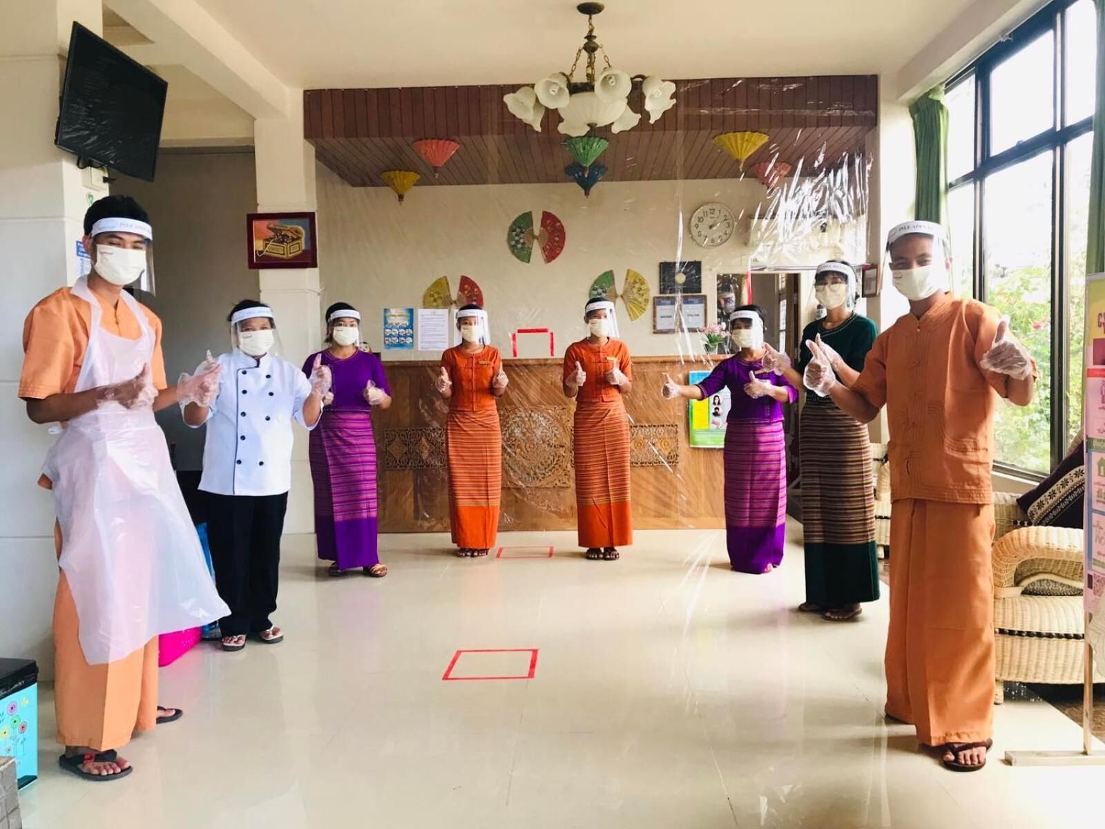 Un groupe de personnes, vêtues de costumes traditionnels, se tient dans une pièce dotée d’un plancher en bois, d’un lustre et d’une grande fenêtre.