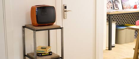 A room with a wooden floor, a metal shelf with a bag of rice, a vintage television, and a door with a modern lock.