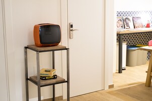 Une pièce avec un plancher en bois, une étagère en métal sur laquelle se trouve un sac de riz, un téléviseur ancien et une porte dotée d’une serrure moderne.