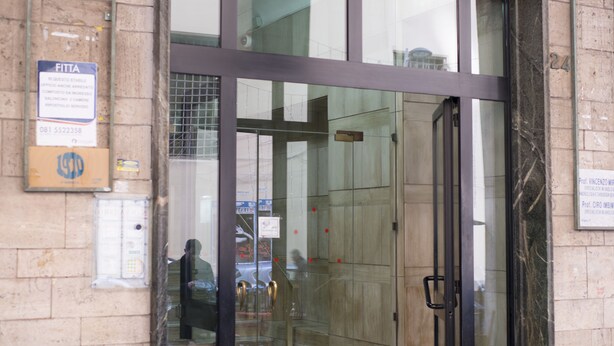 A building entrance with a glass door, a signboard, and a marble wall. - 1970 Rooms (Naples)