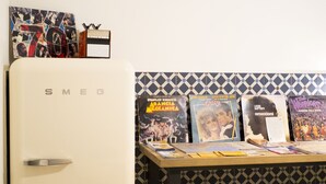 A kitchen with a white Smeg refrigerator, a tiled backsplash, and a table with various items including books and a framed picture. - 1970 Rooms (Naples)