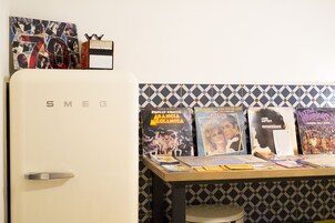 Una cocina con un refrigerador blanco Smeg, salpicadero de azulejos y una mesa con varios objetos, entre ellos libros y un cuadro enmarcado.