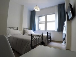 Habitación de hotel con dos camas, un escritorio, una silla, un televisor y una ventana con cortinas.