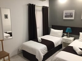 Quarto de hotel com duas camas, uma mesa de cabeceira com abajur, um espelho e um quadro na parede.