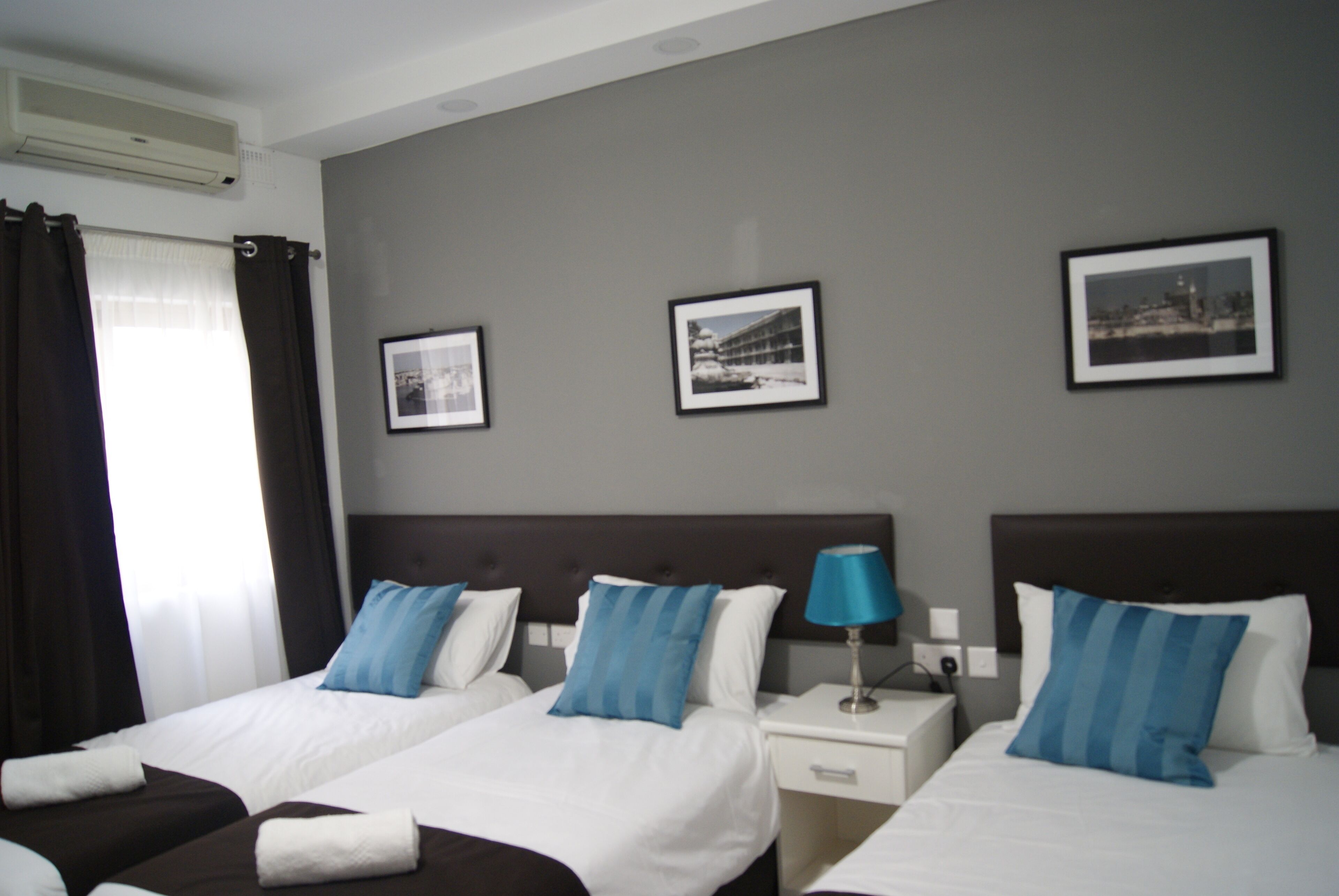A hotel room with two beds, a nightstand with a lamp, and three framed pictures on the wall.