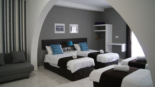 Ein Hotelzimmer mit zwei Betten, einem Schlafsofa, einem kleinen Tisch und einem an der Wand befestigten Regal.