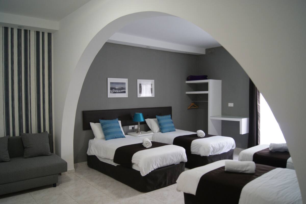 Habitación de hotel con dos camas, un sofá, una mesita y un estante en la pared.