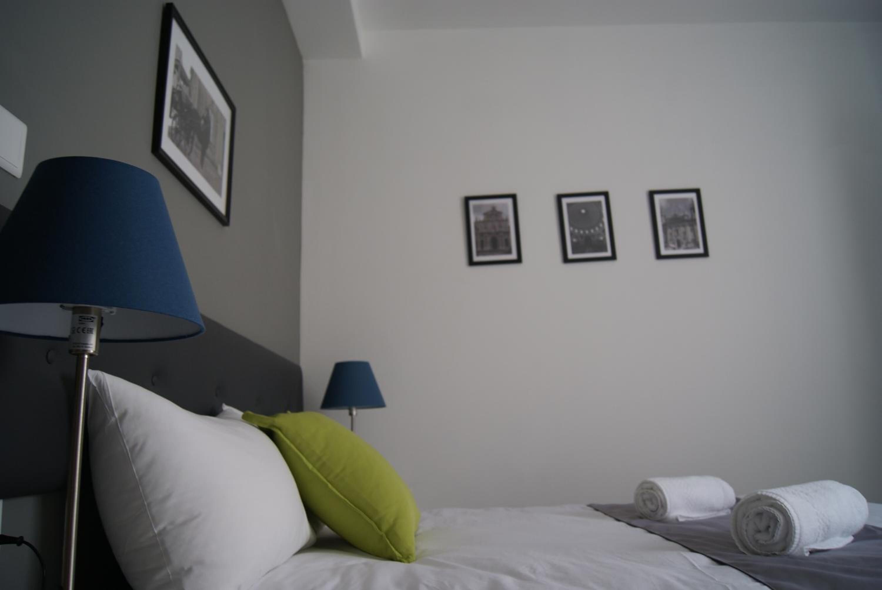 Una habitación de hotel con una cama, dos lámparas, un almohadón y tres cuadros en la pared.