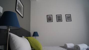 Una habitación de hotel con una cama, dos lámparas, un almohadón y tres cuadros en la pared.