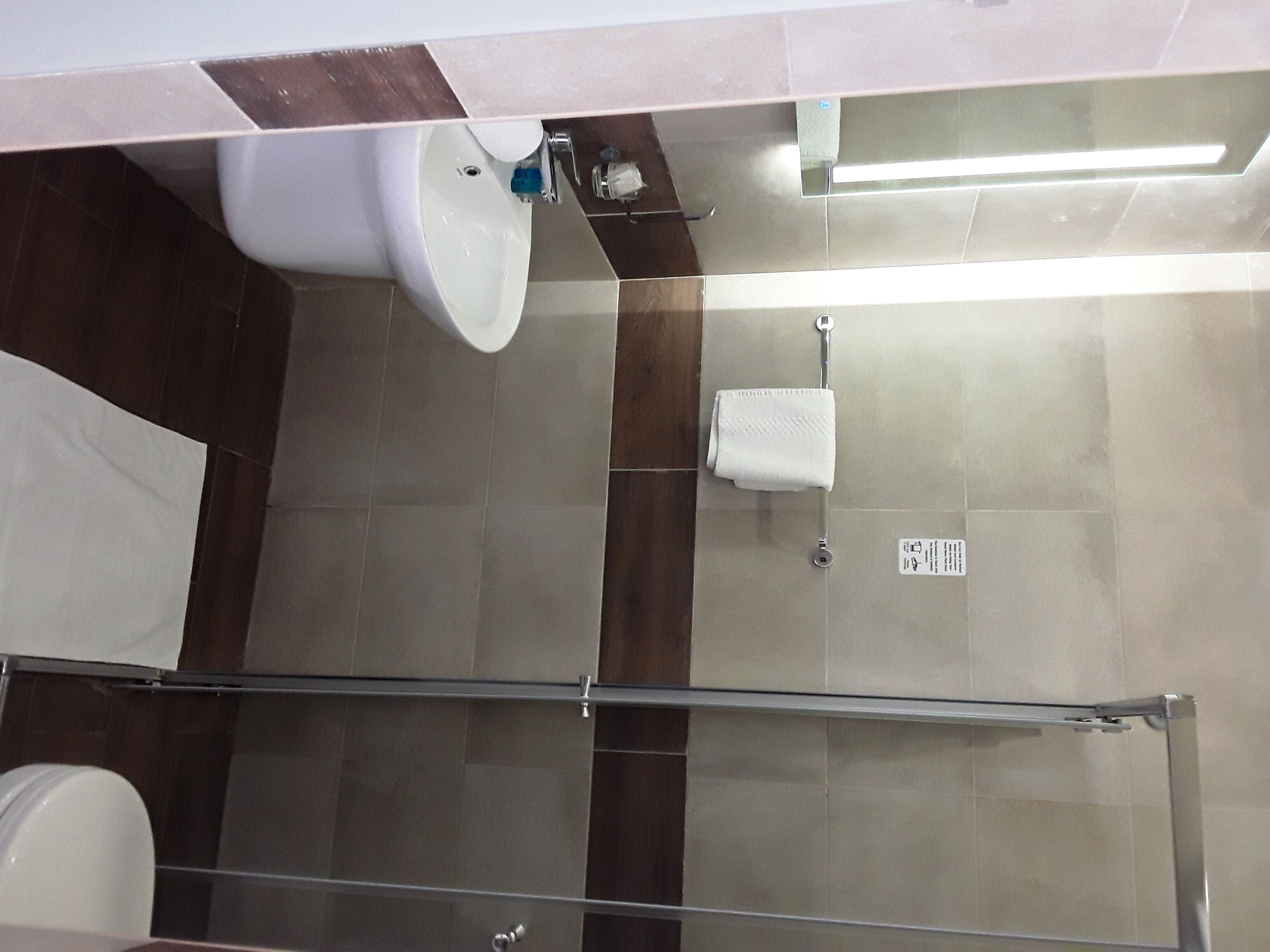Een badkamer met een douchecabine van glas, een wit wastafeltje en een handdoekrek.