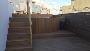 Eine Holzterrasse mit Stufen zu einer Sitzgelegenheit, umgeben von einem niedrigen Zaun und einem Blumentopf.