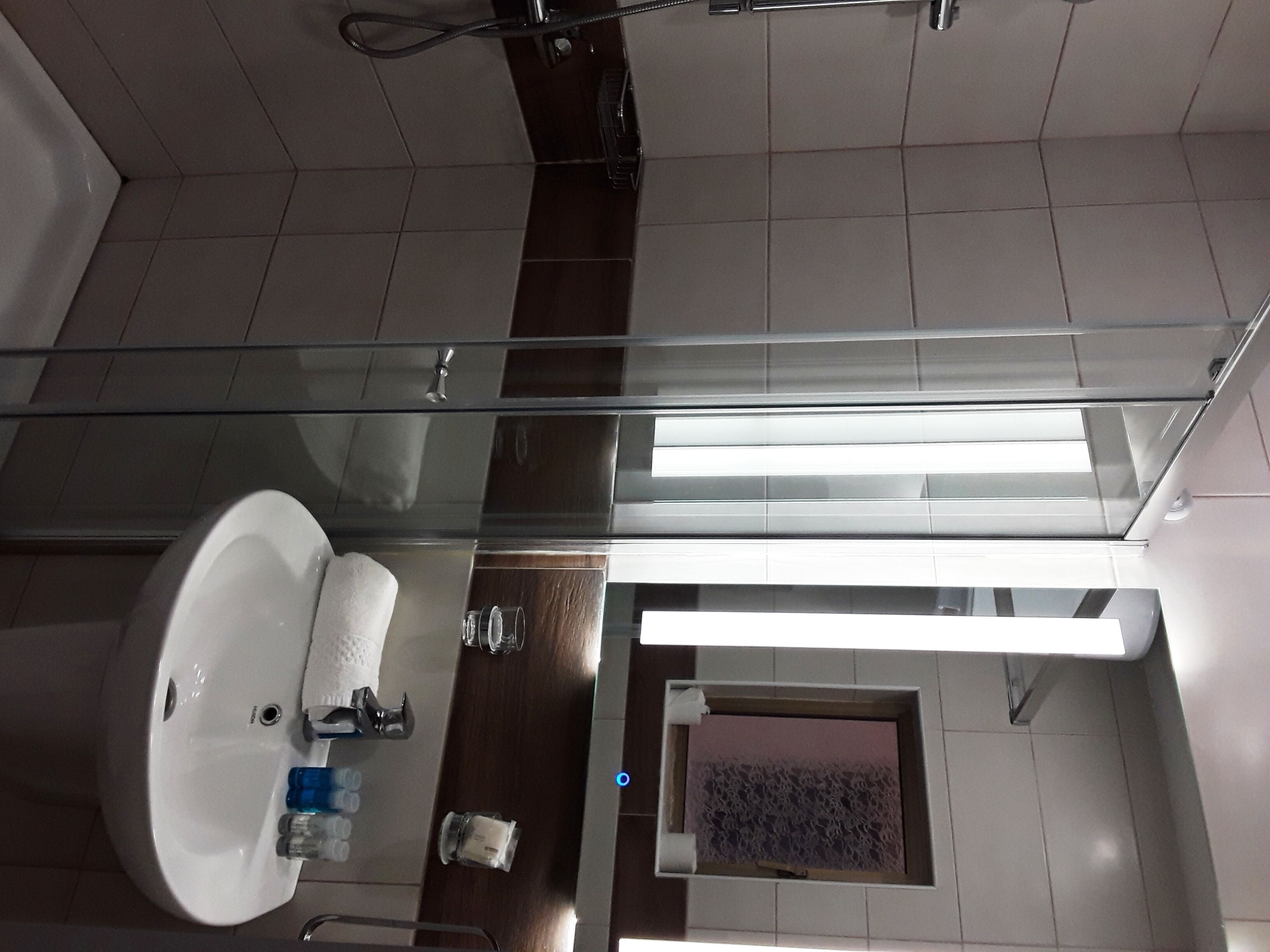 Un baño moderno con cabina de ducha de vidrio, un lavabo blanco y un mueble de tocador de madera.