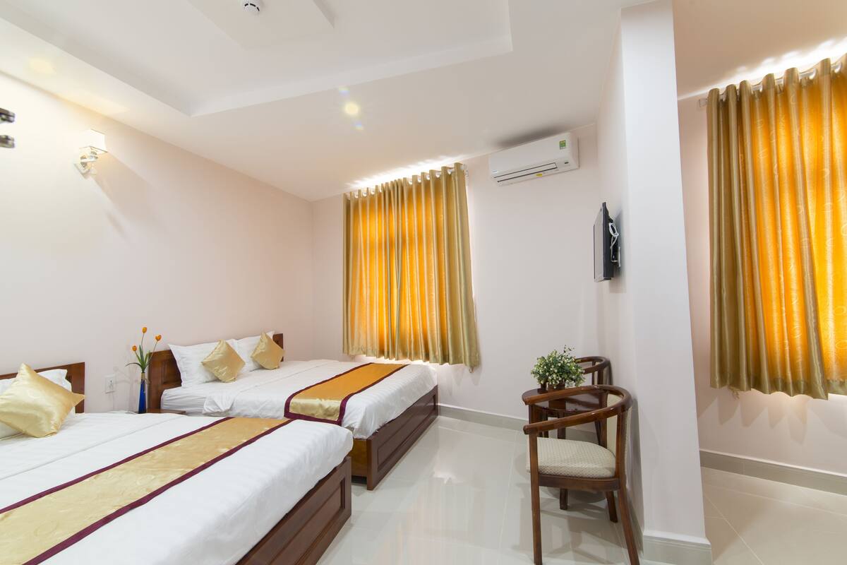 A hotel room with two beds, a chair, a small table, and a wall-mounted TV.