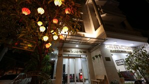 The entrance of the Thuan Ha Hotel with a signboard, illuminated by hanging lanterns, and a visible car parked in front.