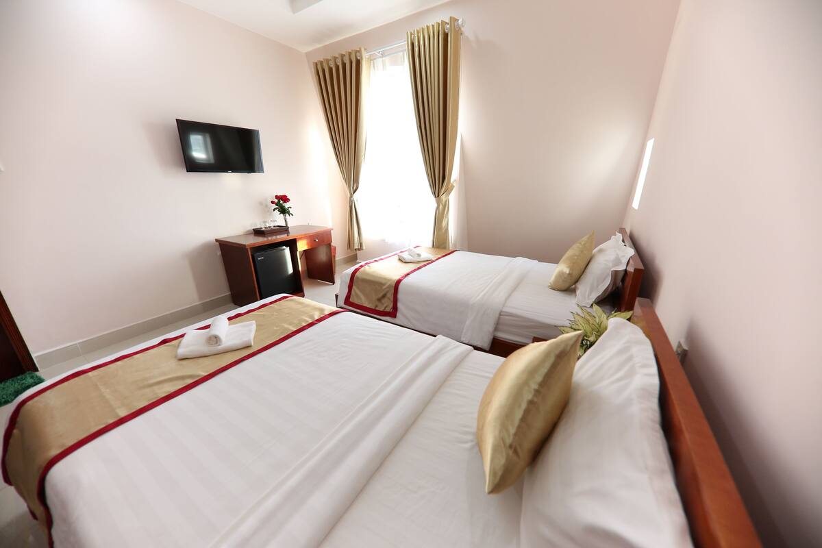 A hotel room with two beds, a TV, a desk, and a window with curtains.